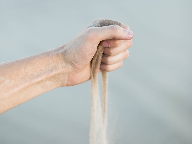 Sand fliesst durch eine ausgestreckte Hand.